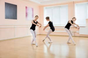 Three young women in black and white outfits practicing dance moves.