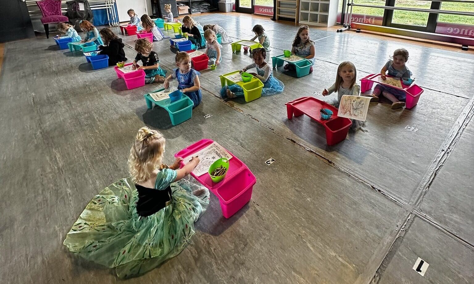 Girls in dresses color at small tables.