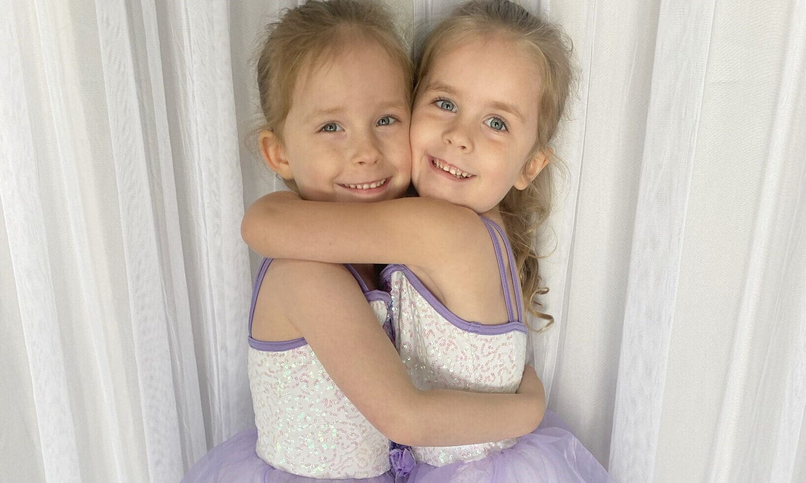 Two girls in purple dresses hugging.