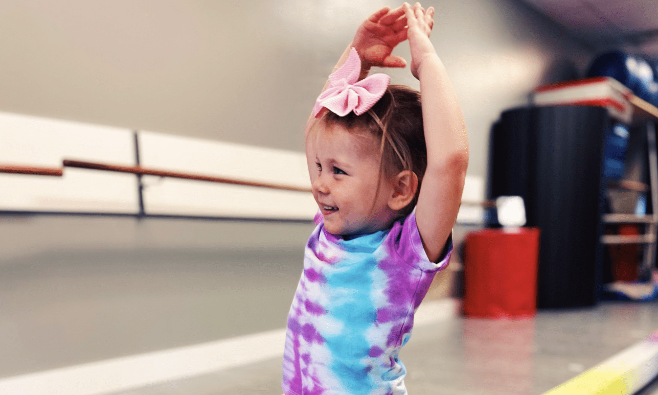 Smiling girl in tie-dye shirt stretches in gym.