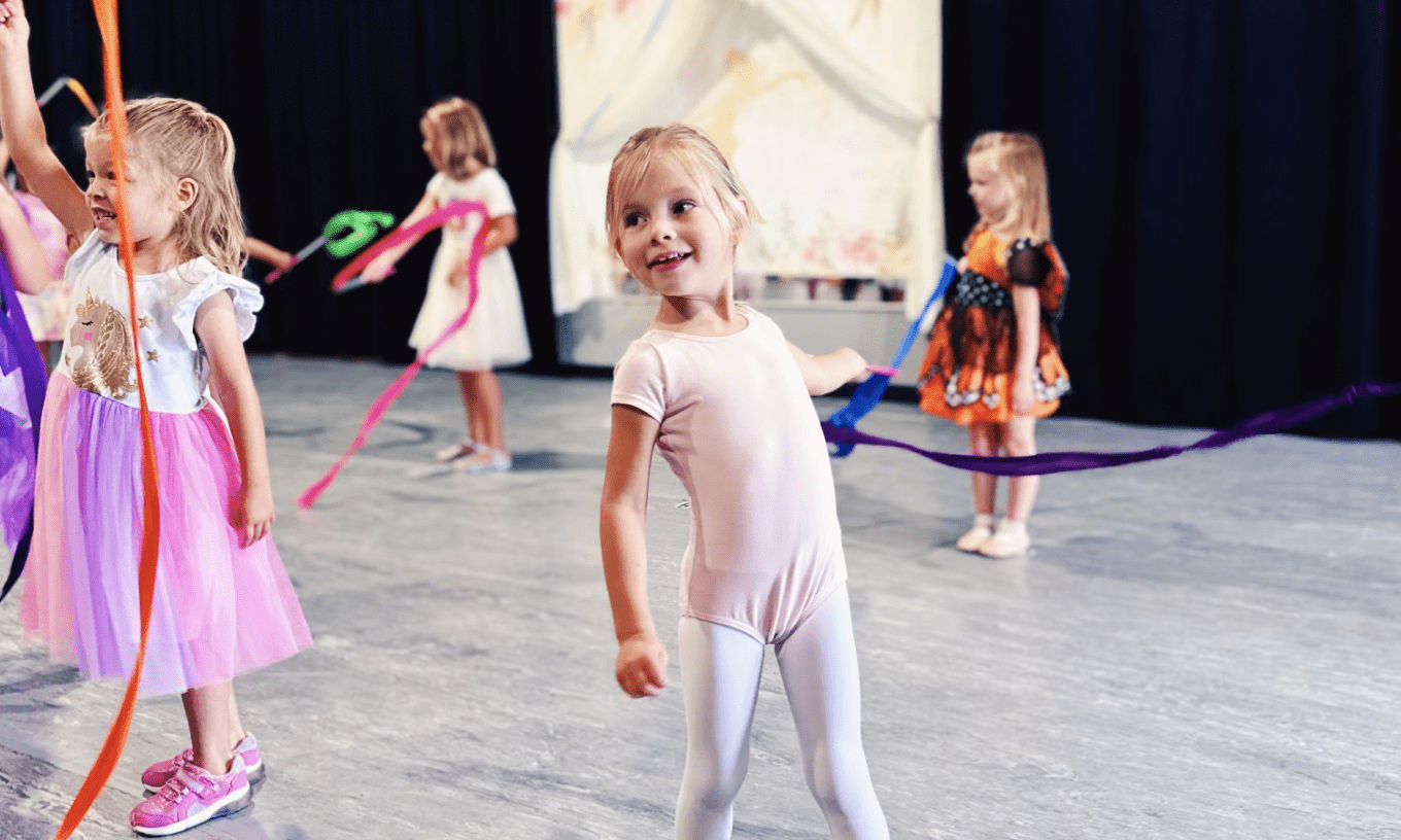 Young girl in pink leotard twirling ribbon.