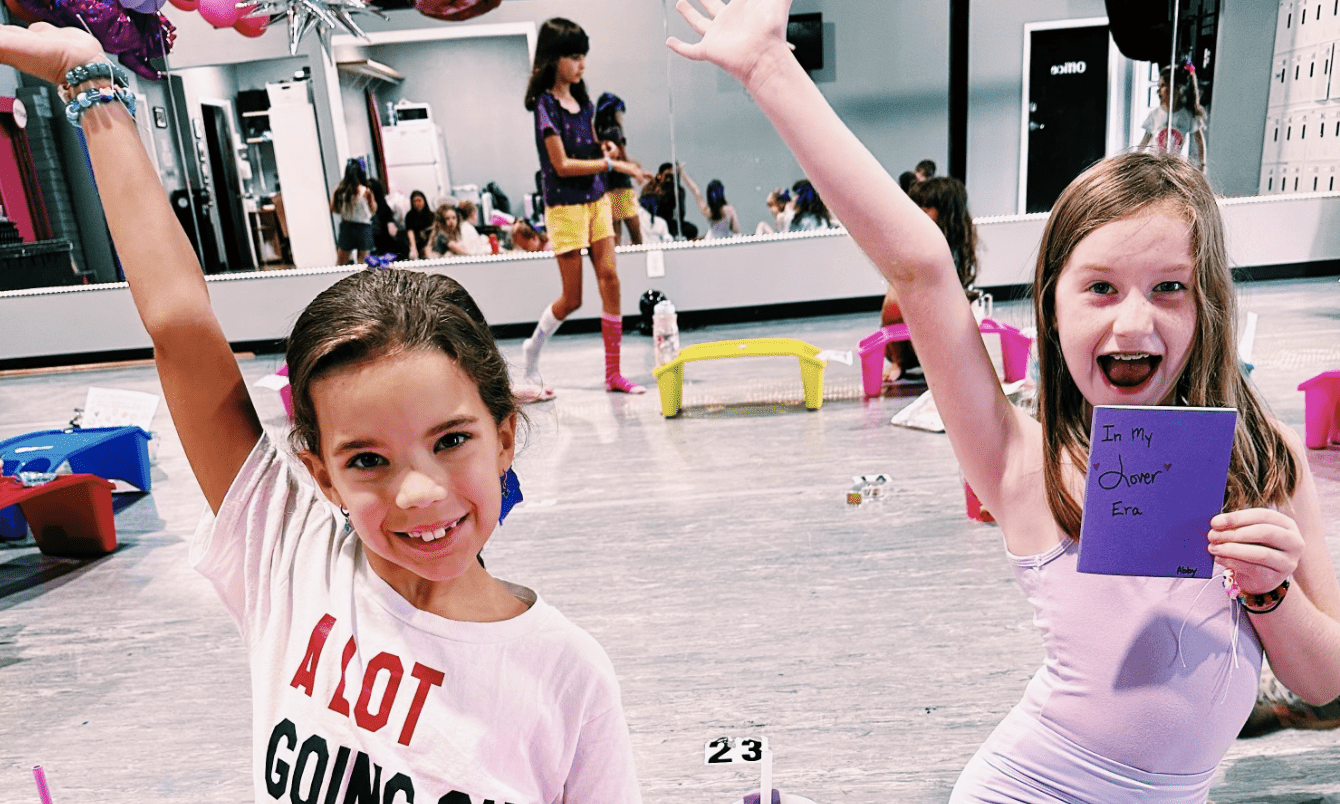 Two girls holding signs smiling in a dance studio.